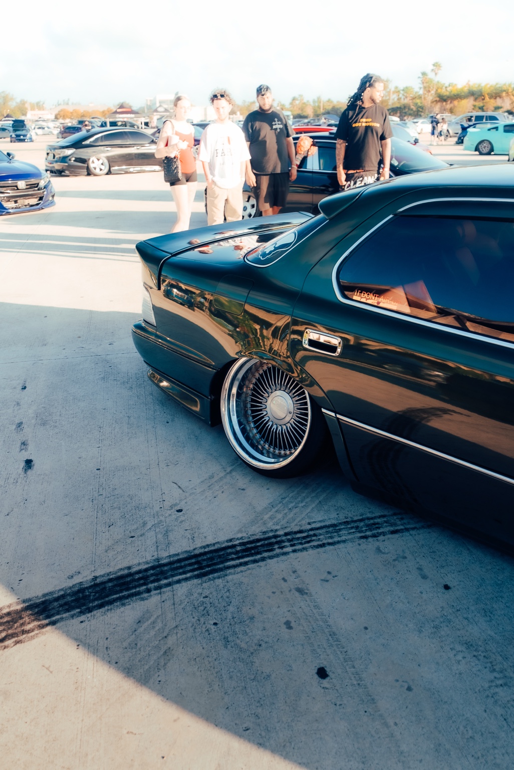A lowered black Lexus at an ASM car meet with attendees in the background